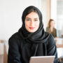 Arab businesswoman at work. Young Arab female in business office holding digital tablet. She is wearing traditinal Emirati Middle Eastern